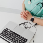 Laptop mit Person die davor sitzt die medizinische Kleidung an hat